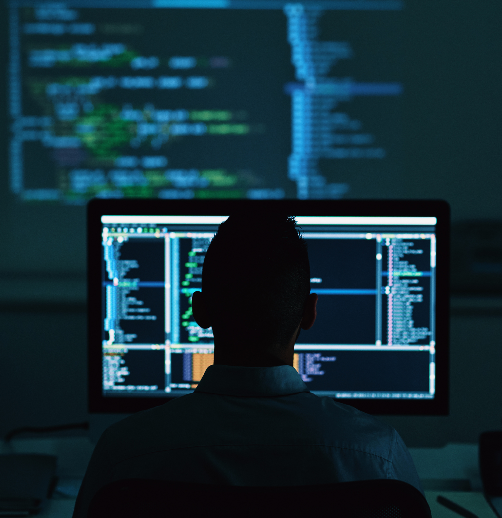 Silhouette of person viewing computer code on dark screen.